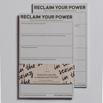 Two Reclaim Your Power notepads stacked with a beige wrap featuring black handwritten script around the lower portion.