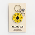 Reclamation spinner enamel keychain attached to a beige display card with a yellow segmented wheel and black droplet centerpiece