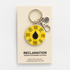 Reclamation spinner enamel keychain attached to a beige display card with a yellow segmented wheel and black droplet centerpiece