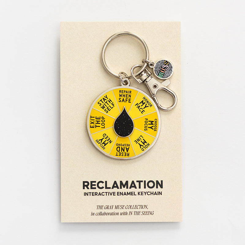 Reclamation spinner enamel keychain attached to a beige display card with a yellow segmented wheel and black droplet centerpiece