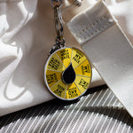Close-up of Reclamation spinner enamel keychain with a yellow wheel and black center, hanging from a metal clasp against light fabric
