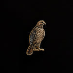 Red-tailed hawk enamel pin with a gold outline and speckled chest on a black background