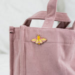 Rosy Maple Moth enamel pin attached to a pink corduroy tote bag.