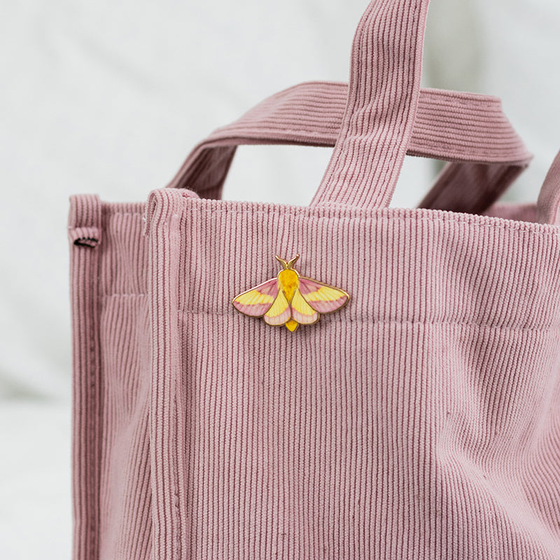Rosy Maple Moth enamel pin attached to a pink corduroy tote bag.