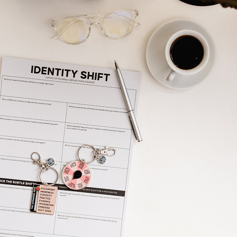 Safe to be Seen Bundle on a white desk with Identity Shift Notepad, spinner, expansion edge slider keychain, coffee, and glasses.