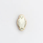 Close up of snowy owl enamel pin against a pale white background