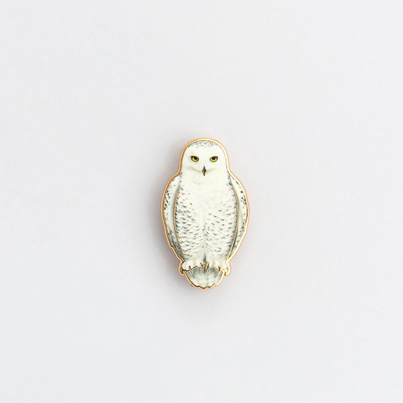 Close up of snowy owl enamel pin against a pale white background