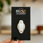 Snowy owl enamel pin with gold edging mounted on a black display card