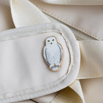 Snowy owl enamel pin attached to a light beige bag with a fabric strap