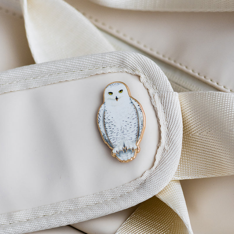 Snowy owl enamel pin attached to a light beige bag with a fabric strap