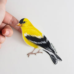 Bright yellow goldfinch matte sticker held between fingers against a white background.