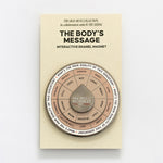 The Body's Message interactive enamel magnet with a circular segmented spinner on beige packaging.