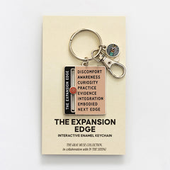 Expansion Edge enamel keychain with pink panel and black edge label on beige display card with keys and a round charm.
