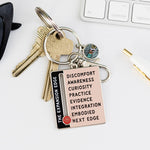 Expansion Edge enamel keychain among desk keys with a keyboard in the background.