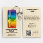 Rainbow gradient enamel keychain with metal ring attached to a cream card showing The Frequency Field.