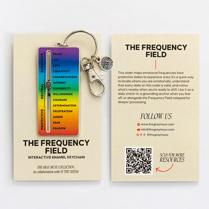 Rainbow gradient enamel keychain with metal ring attached to a cream card showing The Frequency Field.