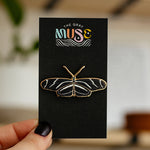 Zebra Longwing butterfly enamel pin on a black display card with The Gray Muse logo held by a hand